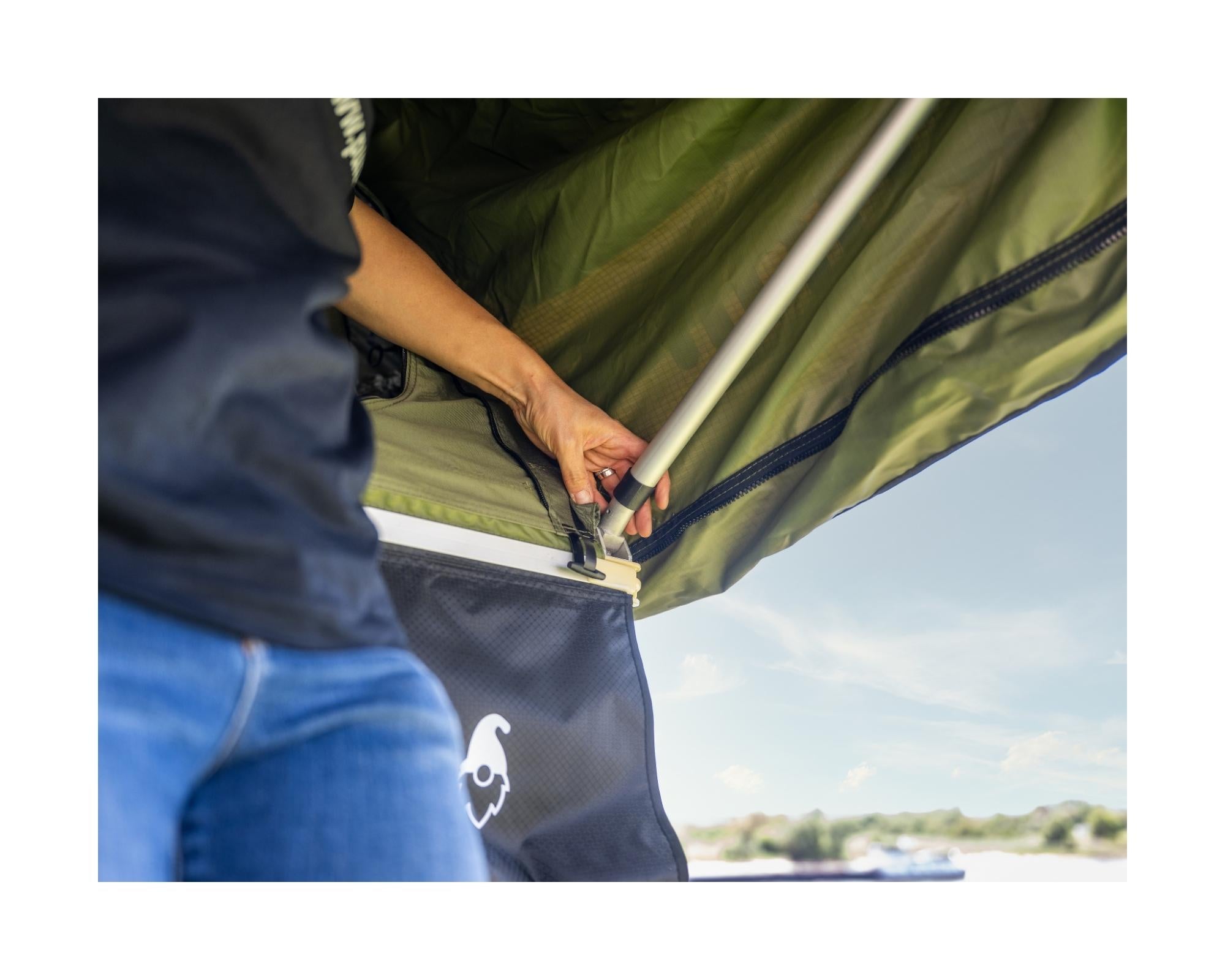 Detailfoto von der Montage der Stange vom Vordach beim grünen Dachzelt. Schwarze Schuhtasche ist zu sehen.
